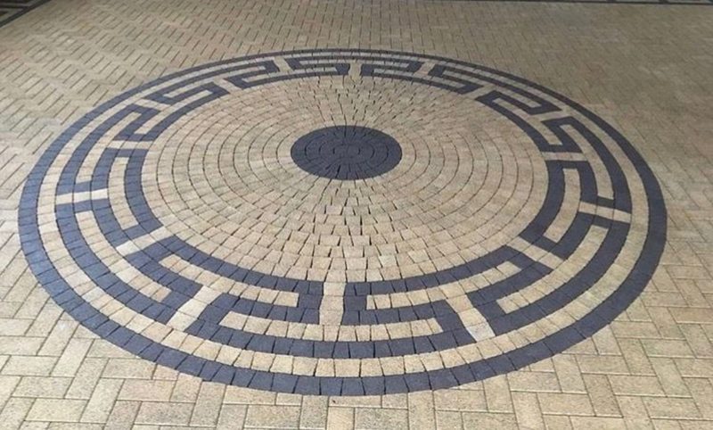 Custom circular paver inlay with a dark Greek-key border set into a herringbone paver field