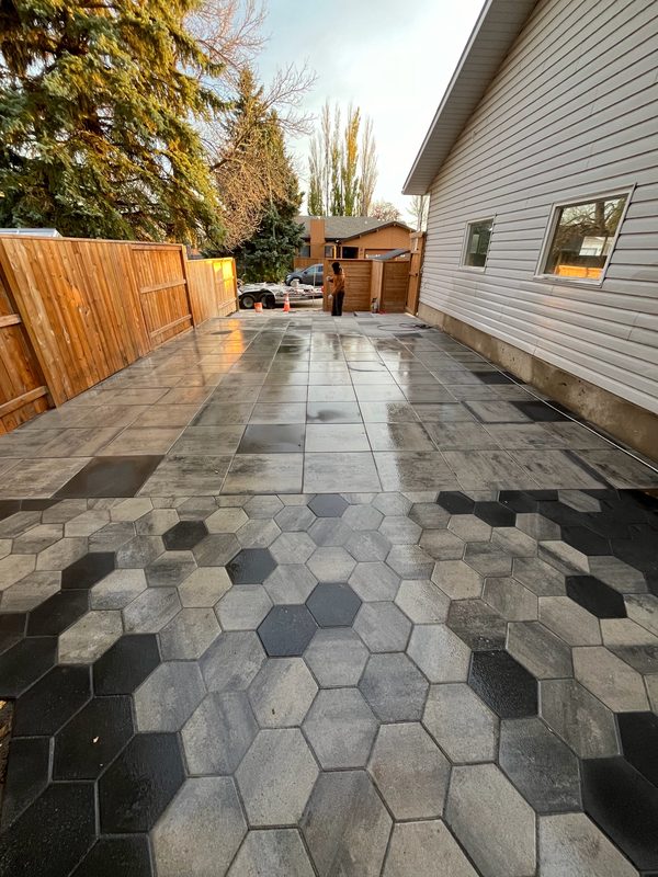 Side-yard patio of large-format grey slabs transitioning into a multi-tone hexagon paver field along a cedar fence
