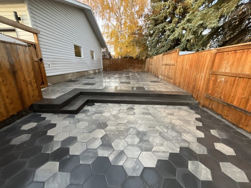Multi-tone hexagon pavers leading to built-in dark stone steps and a large-slab patio beside a cedar fence